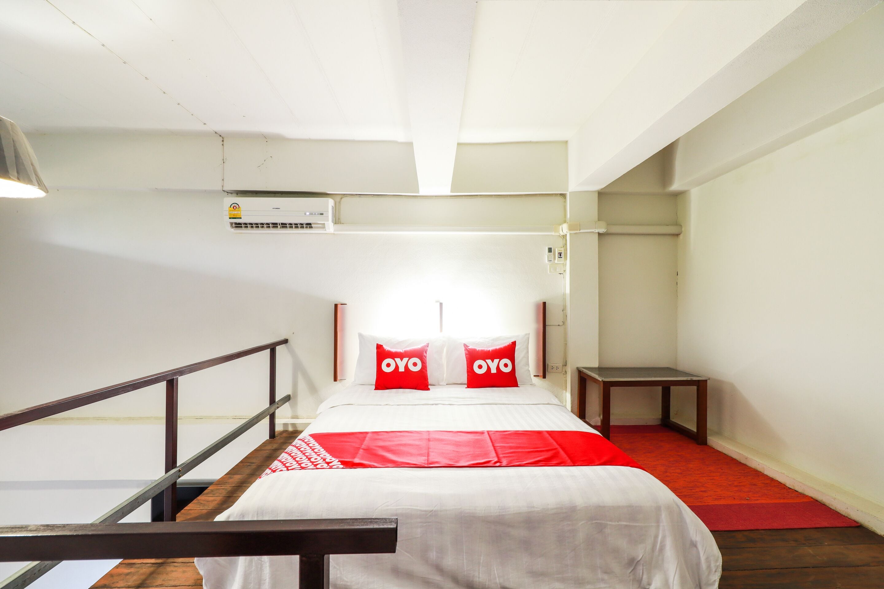 A hotel room with a bed, a small table, and a red carpet.