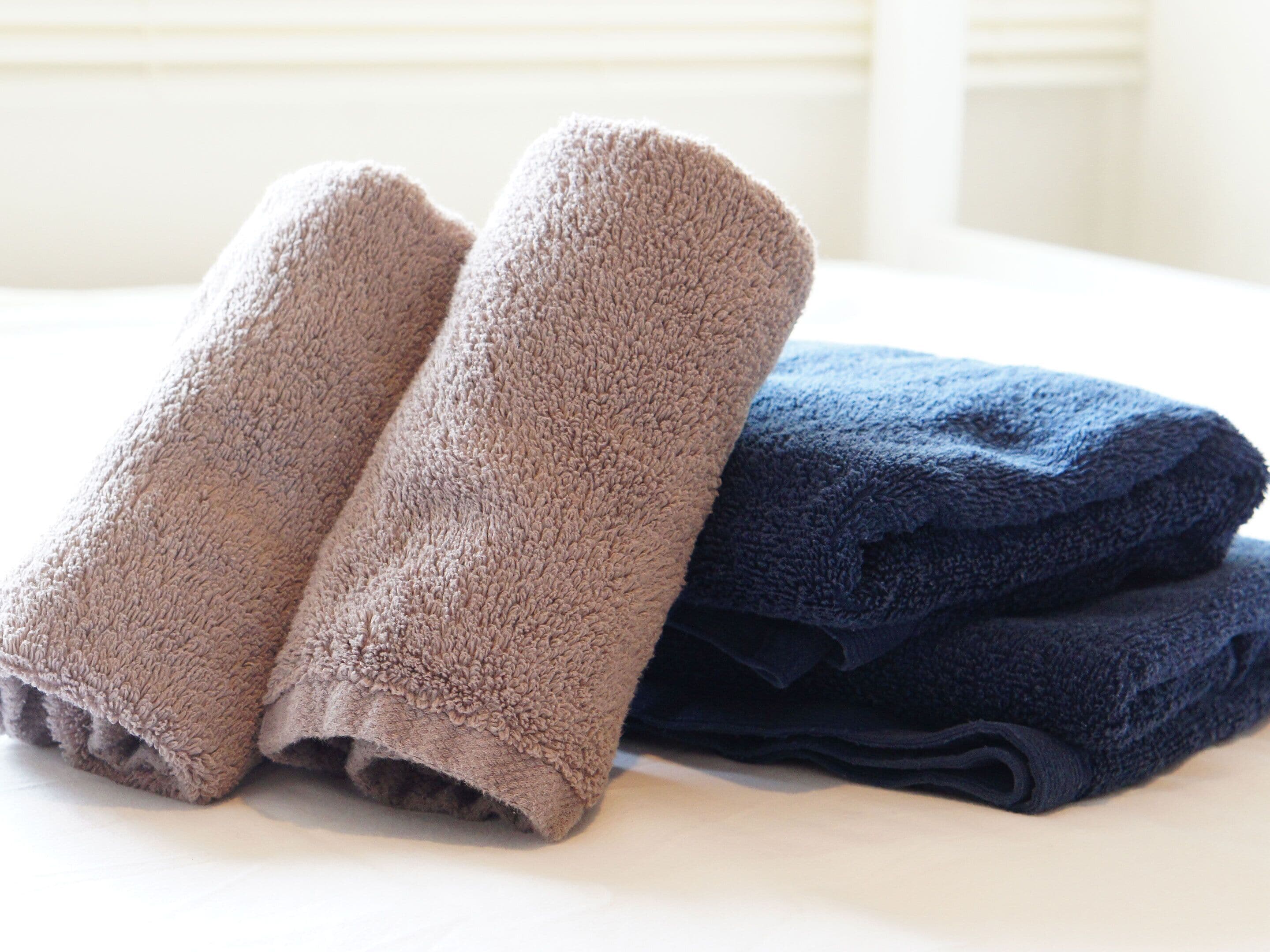 Una cama con dos toallas enrolladas, una beige y otra azul oscuro.