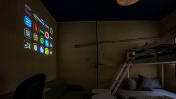 A dimly lit room with a bunk bed, a desk, and a chair. There is a wall with illuminated icons representing various streaming services.