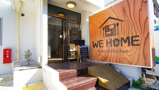 A hostel entrance with a wooden sign reading "WE HOME Hostel & Kitchen".