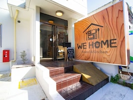 Entrada a un hostal con un letrero de madera que dice "WE HOME Hostel & Kitchen".