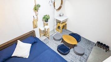 Un dormitorio compacto con cama, un taburete de madera, una mesita redonda y una mesita de noche blanca con espejo.
