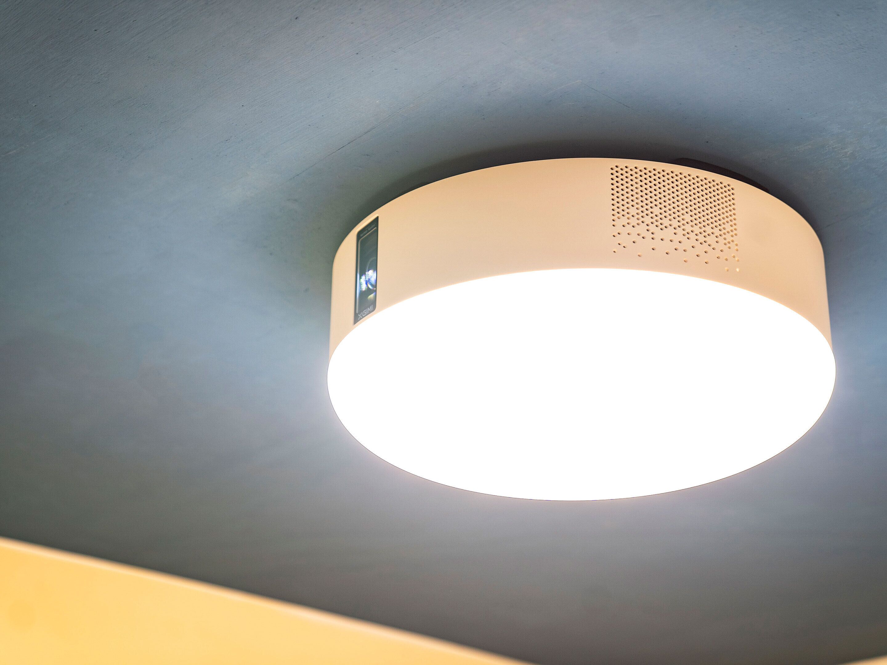 A ceiling-mounted light fixture with a circular design and a small speaker grille.