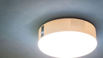 A ceiling-mounted light fixture with a circular design and a small speaker grille.