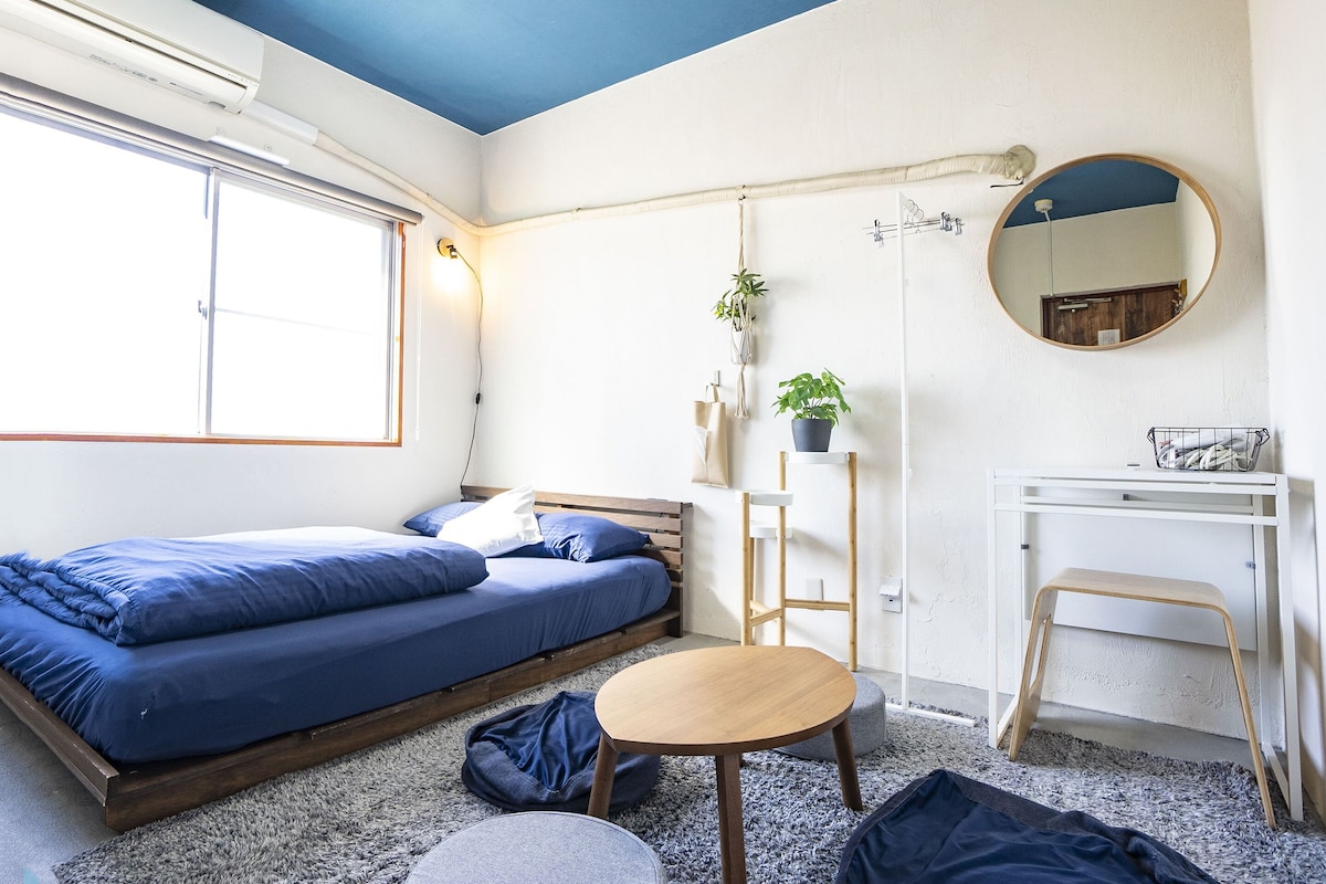 A compact bedroom with a bed, bedside table, chair, and a small desk with a mirror.