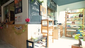 A cozy coffee shop interior with a chalkboard sign reading "Welcome," wooden furniture, and shelves stocked with various items.