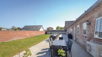 A patio with a table and chairs, a brick wall, and a building with windows and a fan.