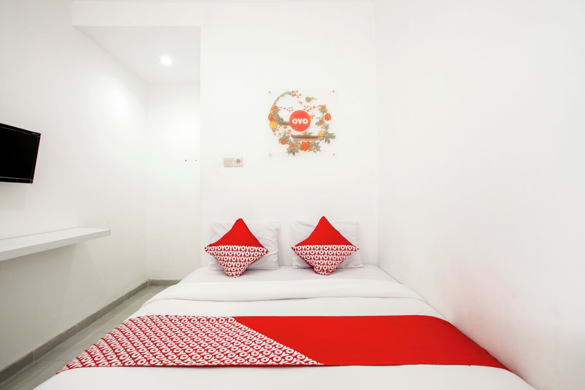 A hotel room with a bed, two pillows, a red blanket, and a wall decoration.