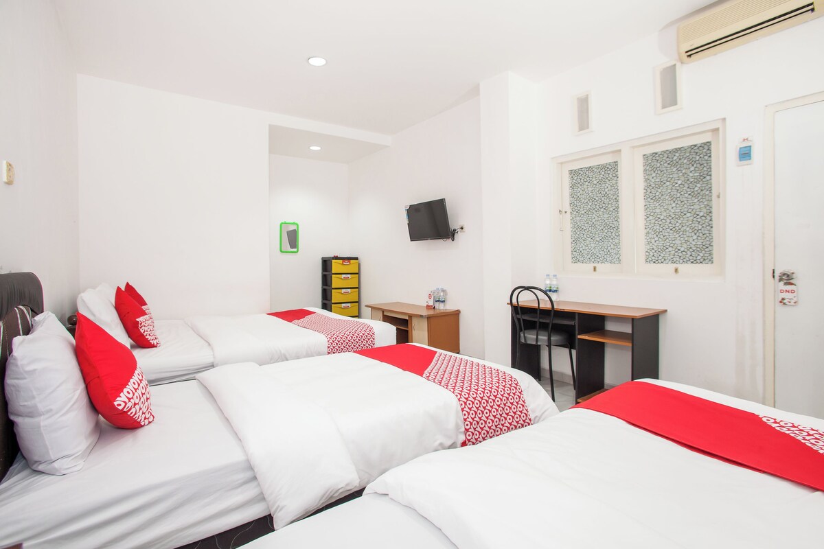 A hotel room with three beds, a desk, a chair, and a TV on the wall.