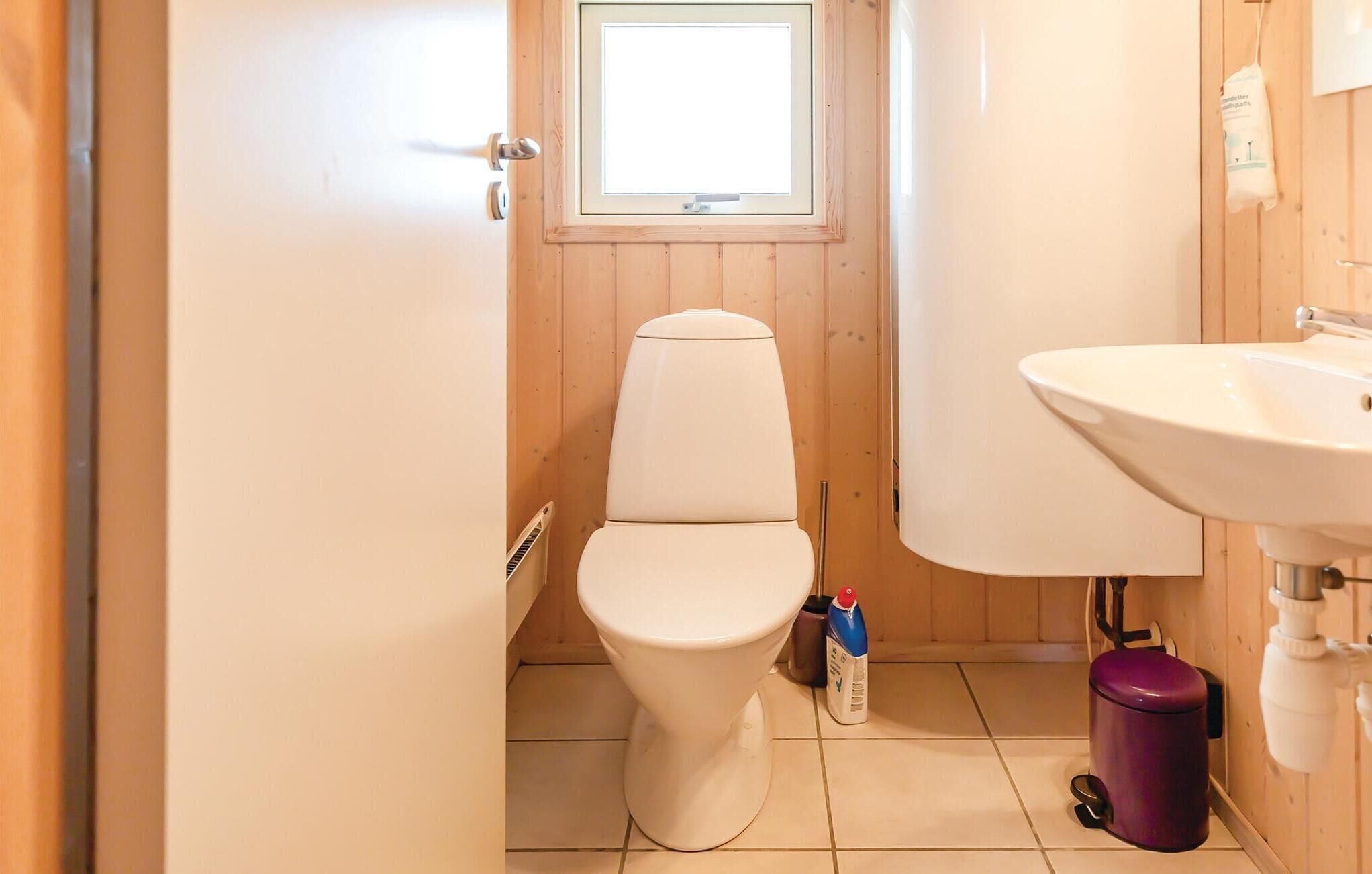 A small bathroom with a toilet, a sink, and a window above the toilet.