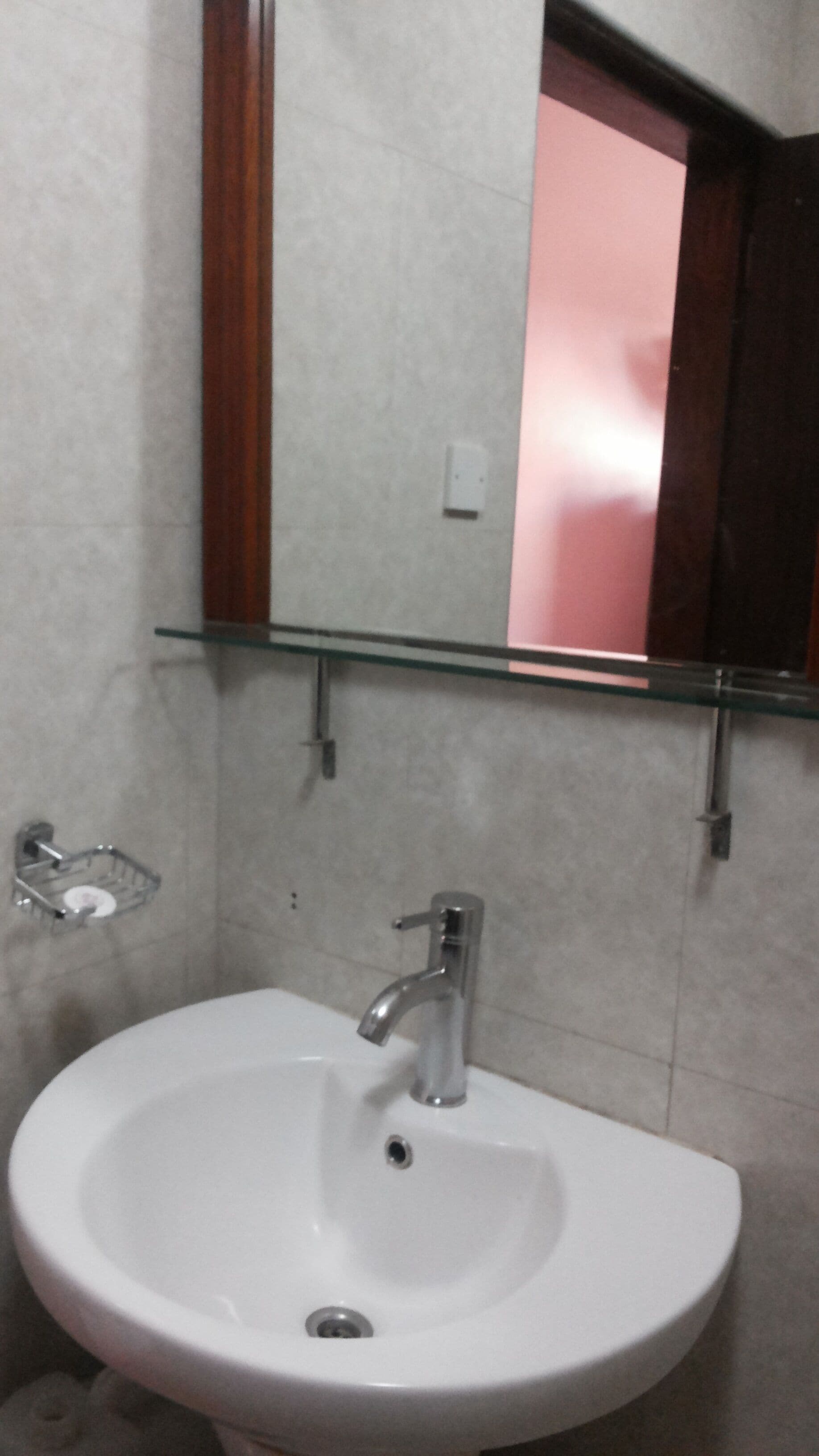 A bathroom with a white sink, a mirror, and a glass shelf above the sink.