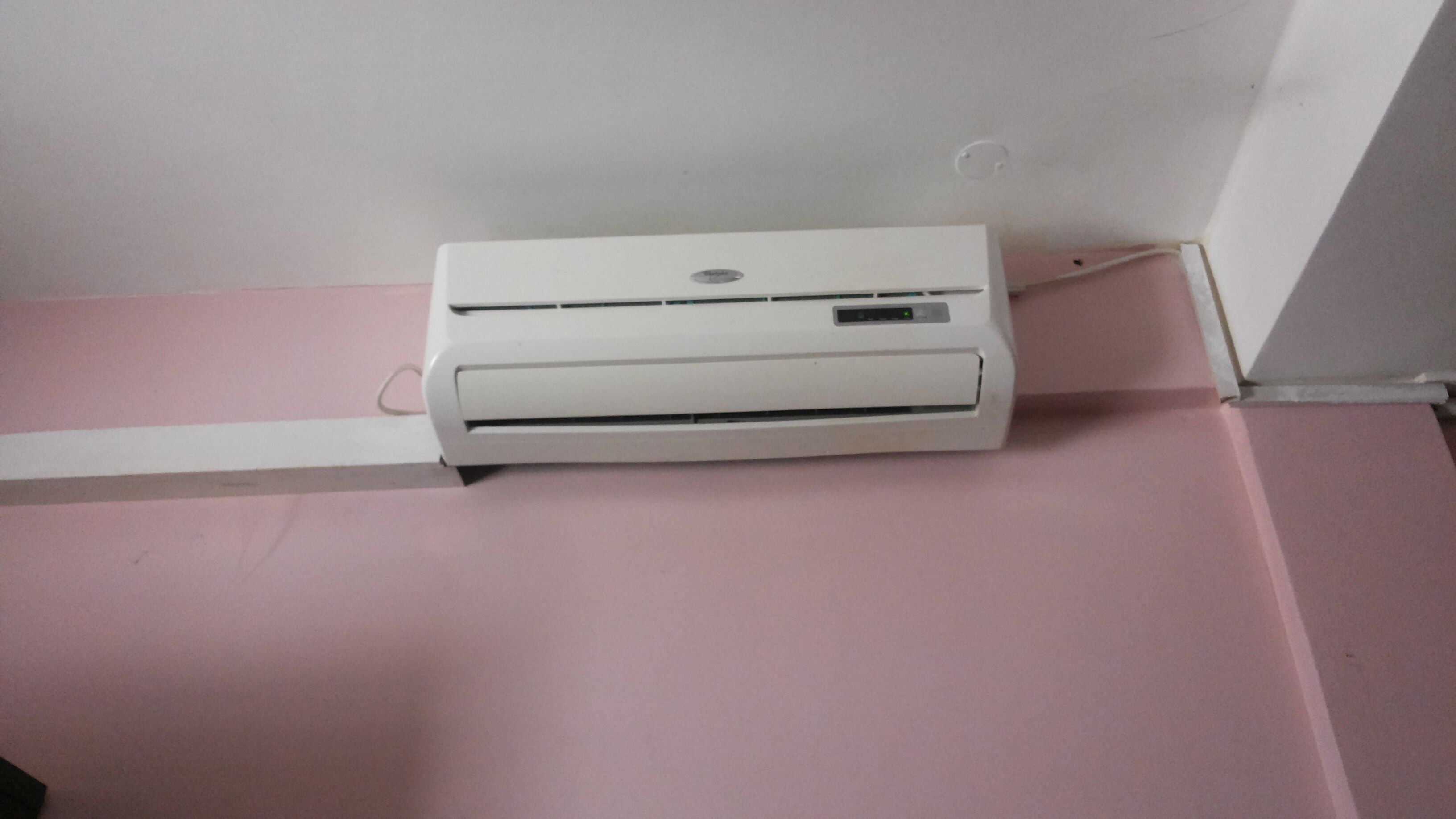 A white air conditioning unit mounted on a pink wall.