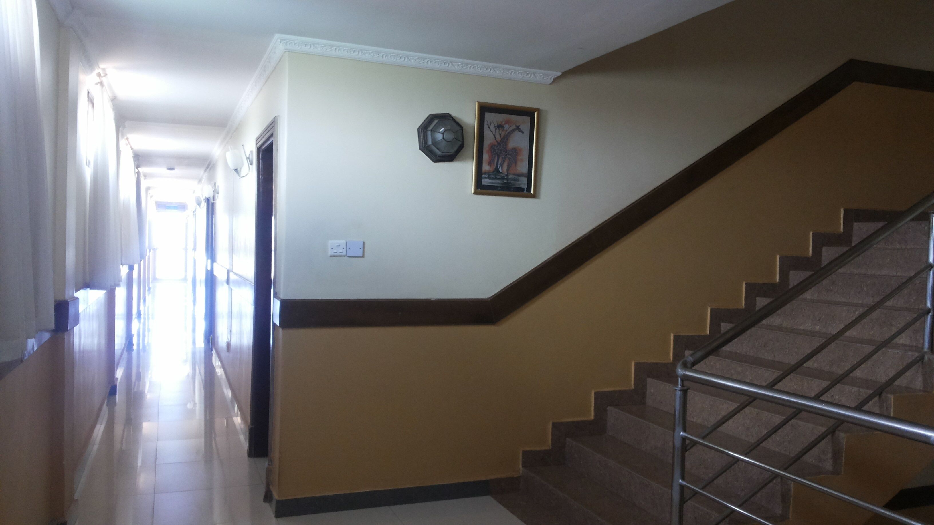 Un pasillo con una escalera, un cuadro enmarcado y una lámpara fijada a la pared.