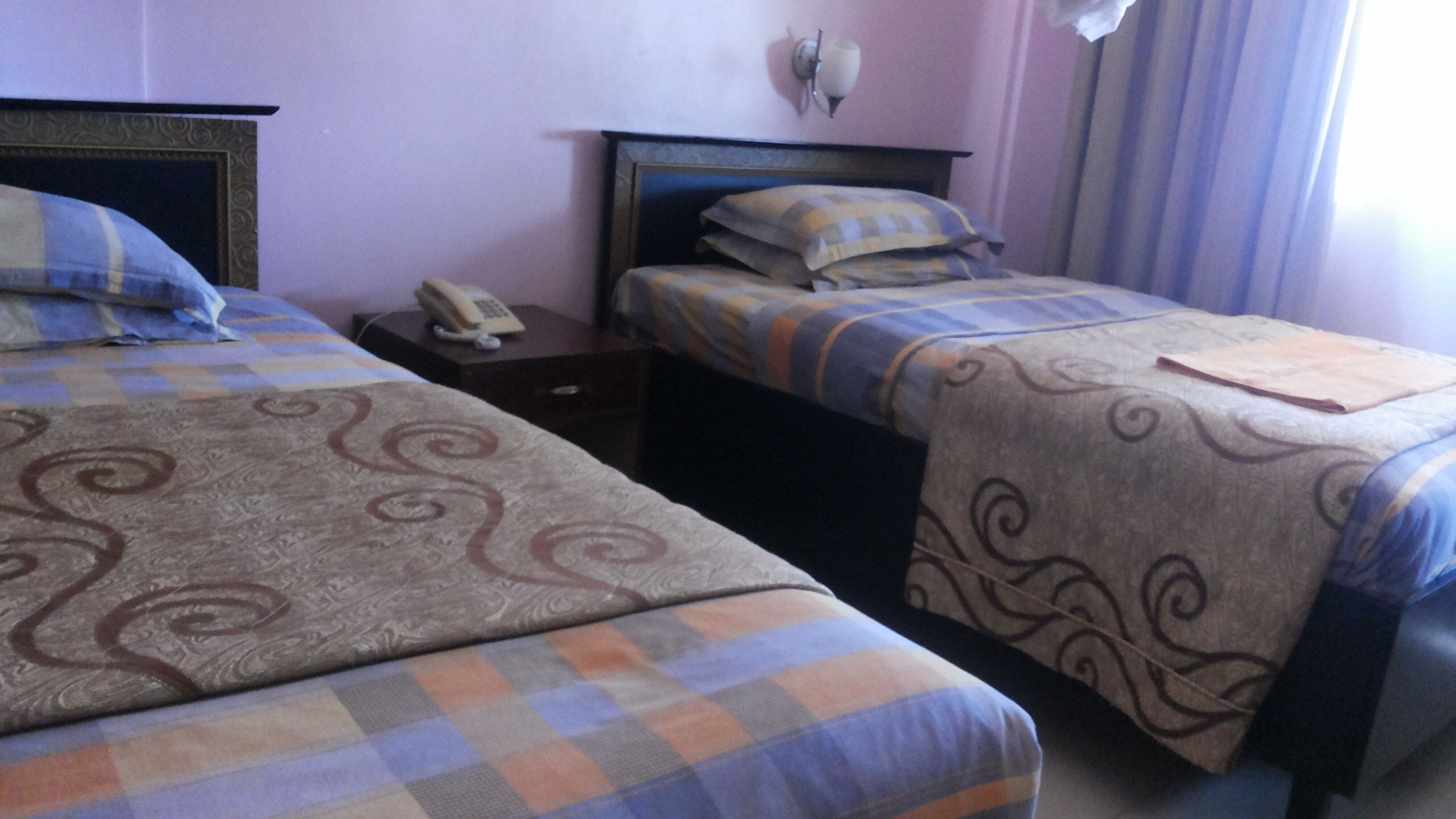 Habitación de hotel con dos camas, cada una con una colcha estampada. Entre las camas, una mesita de noche con un teléfono.