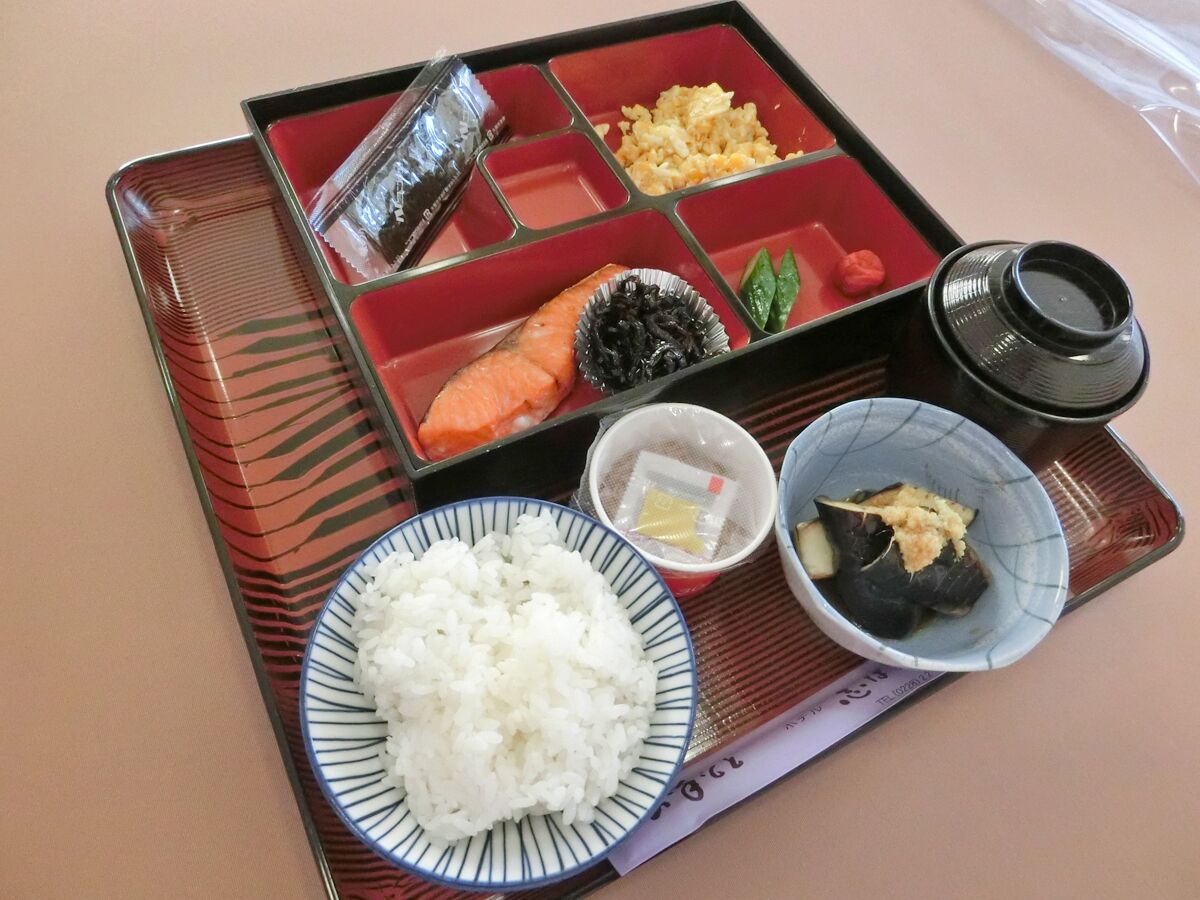 Una caja bento con arroz, salmón, algas marinas y otros ingredientes sobre una bandeja.