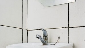 Un lavamanos blanco con grifo de cromo, instalado en una pared con azulejos.