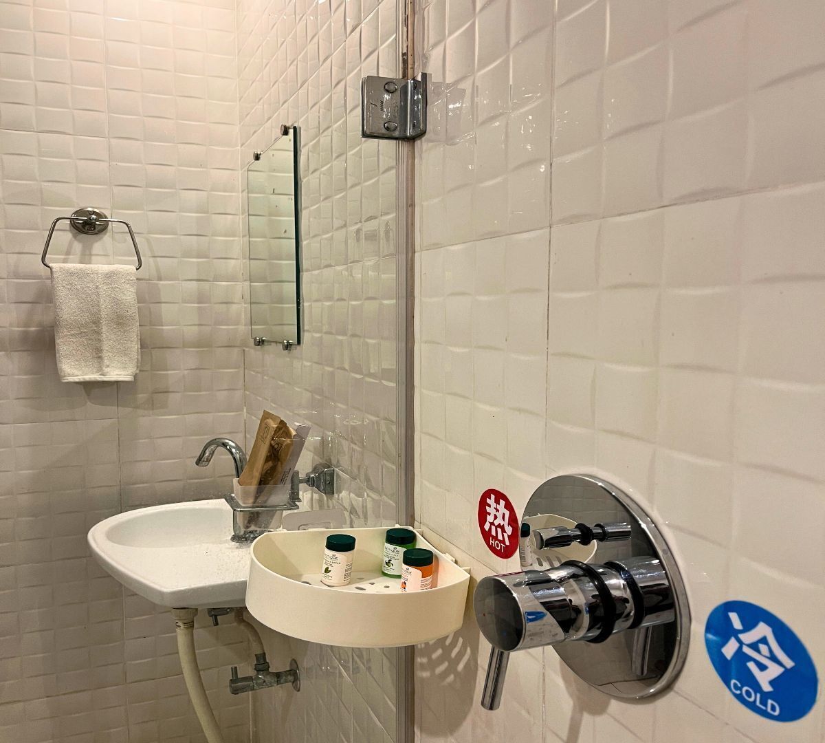 A bathroom with white tiled walls, a sink with a mirror above it, a towel rack, and a soap dispenser.