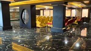 Un salón de conferencias con filas de sillas, suelo de mármol y una araña.