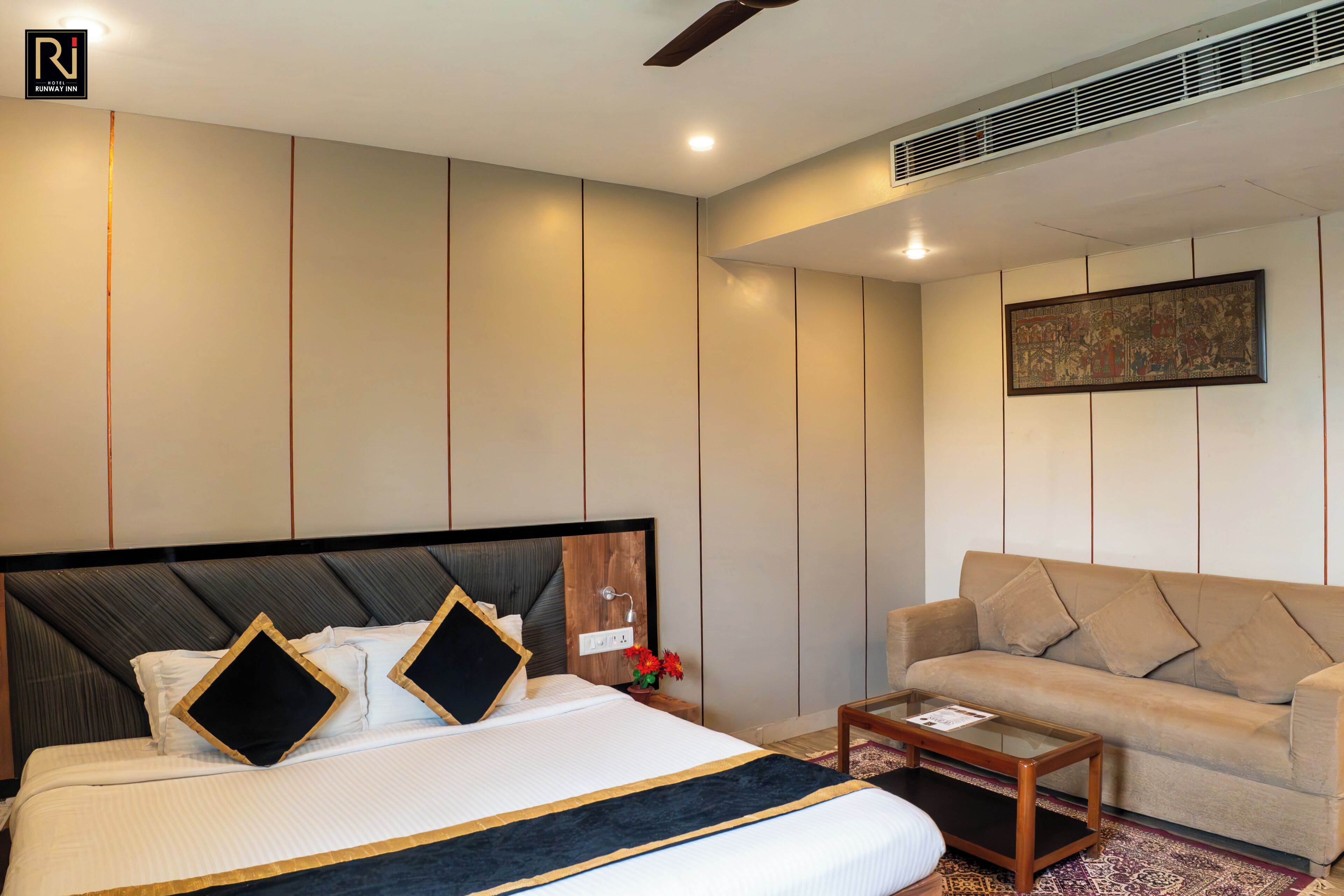 A hotel room with a large bed, a sofa, a small table, and a wall-mounted air vent.