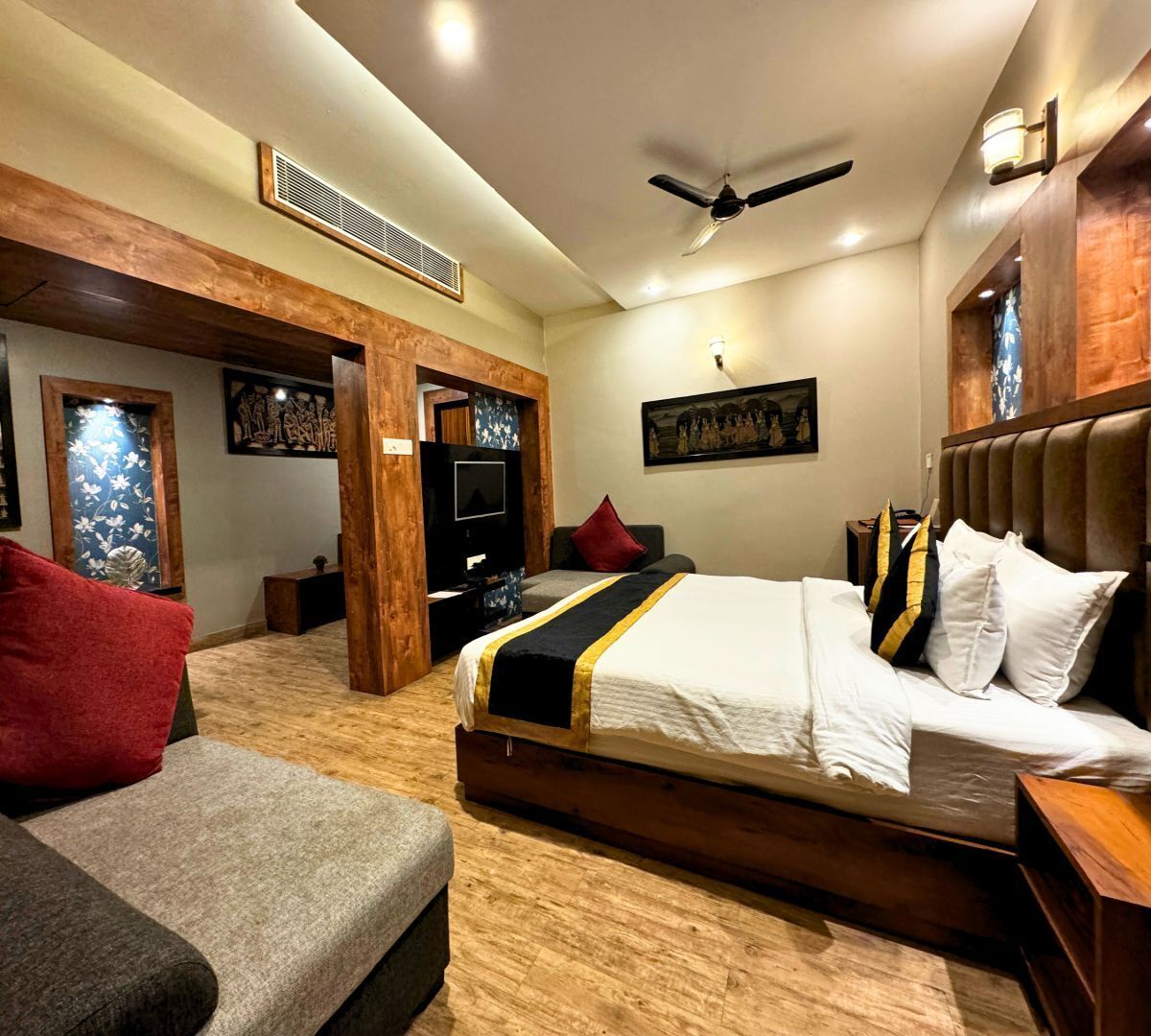 Habitación de hotel con una cama grande, sofá, televisión, detalles de madera y obras de arte en las paredes.