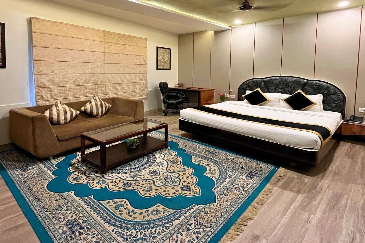 A modern bedroom with a large bed, a sofa, a desk, and a patterned rug.