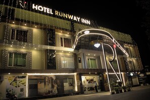 A hotel named "Hotel Runway Inn" with multiple floors, illuminated by string lights and featuring a modern architectural design.