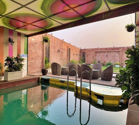 An indoor swimming pool with a colorful ceiling, wicker lounge chairs, and potted plants.