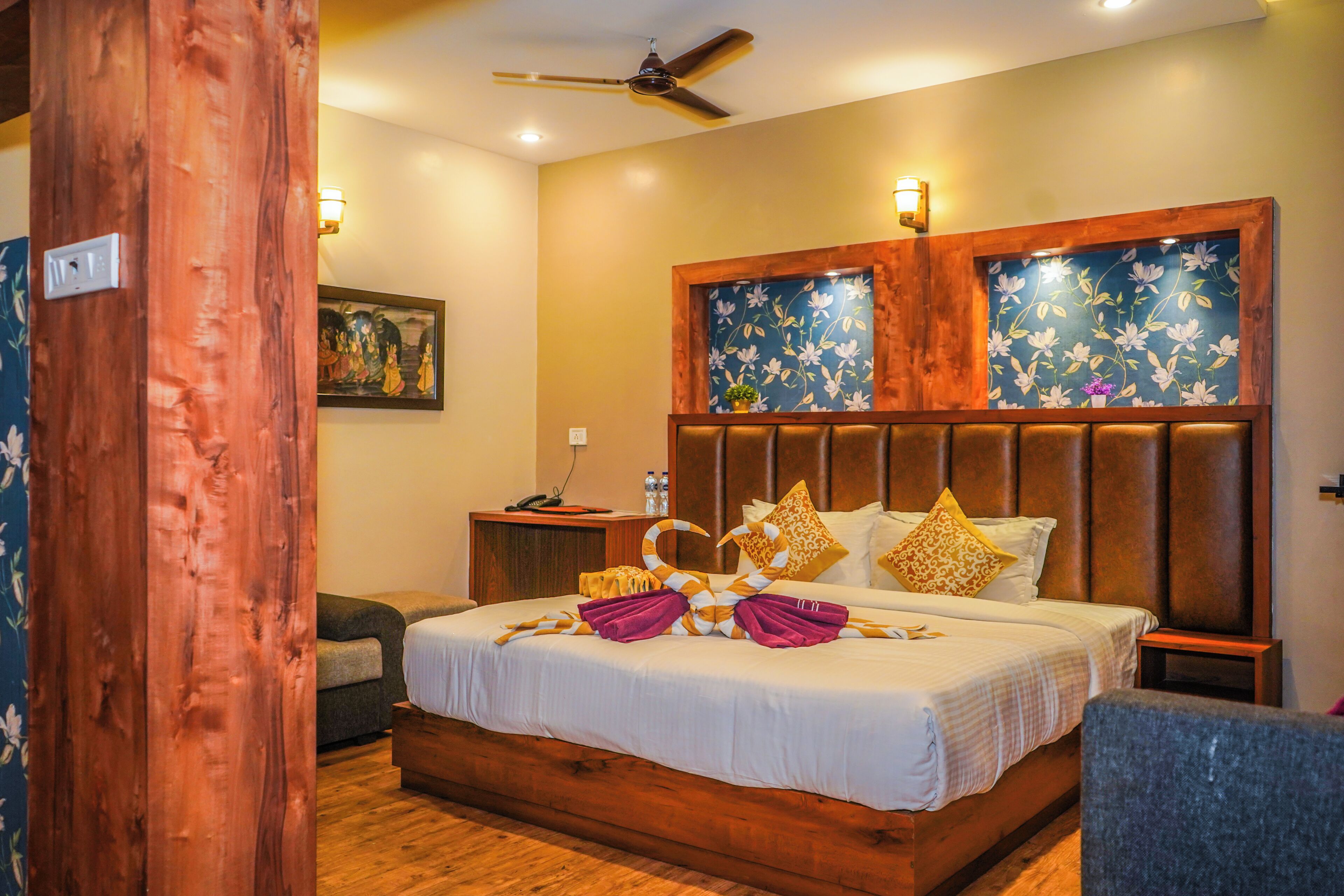 A hotel room with a wooden headboard, a bed with white linens, a nightstand, a desk, and a chair.