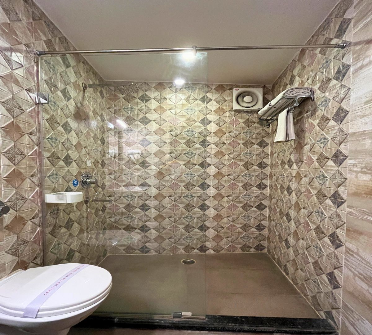 A shower stall with a glass door, a white sink, and a patterned tile wall.