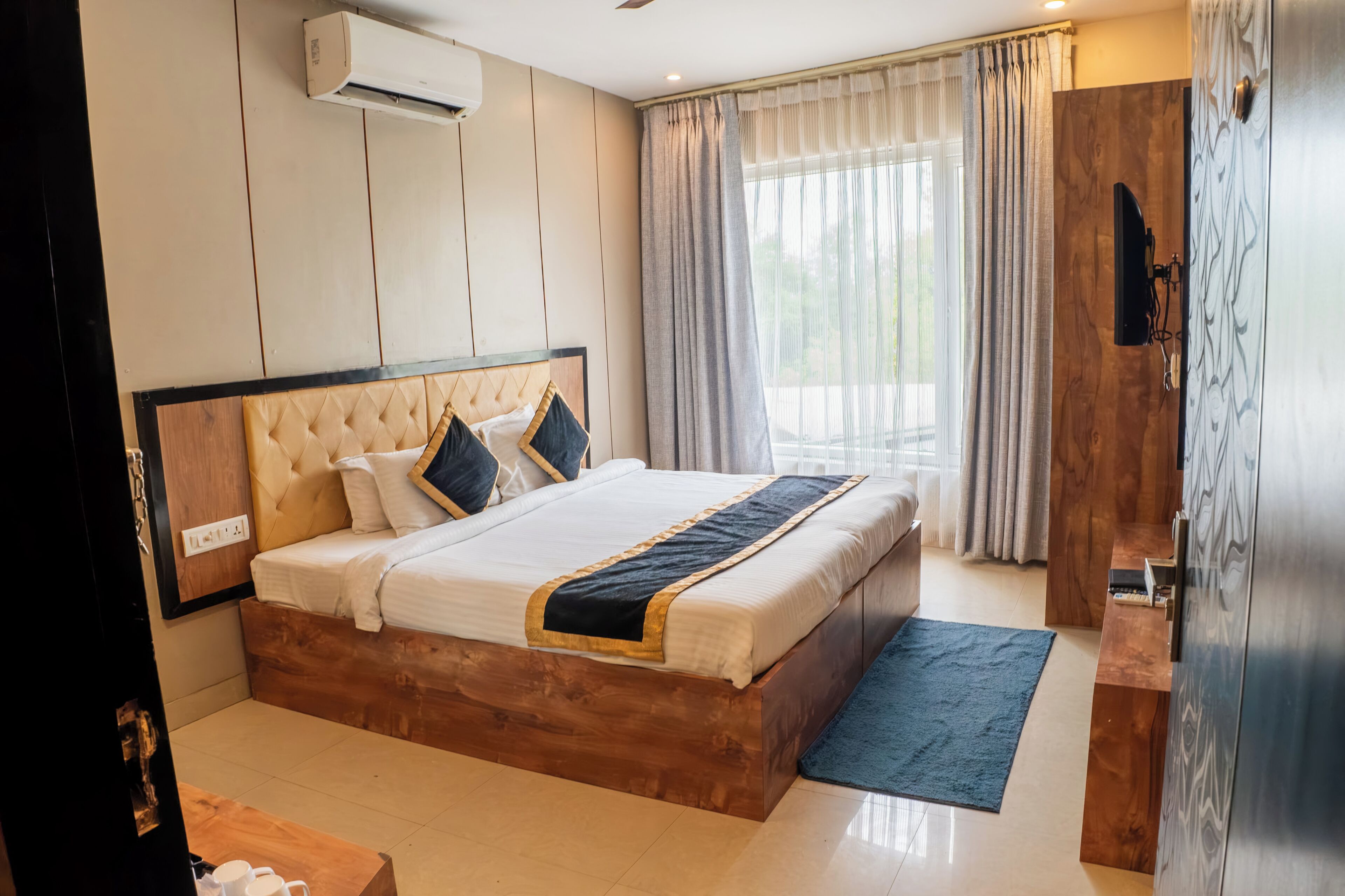 Habitación de hotel con cama de madera, televisor de pantalla plana, armario y ventana con cortinas.