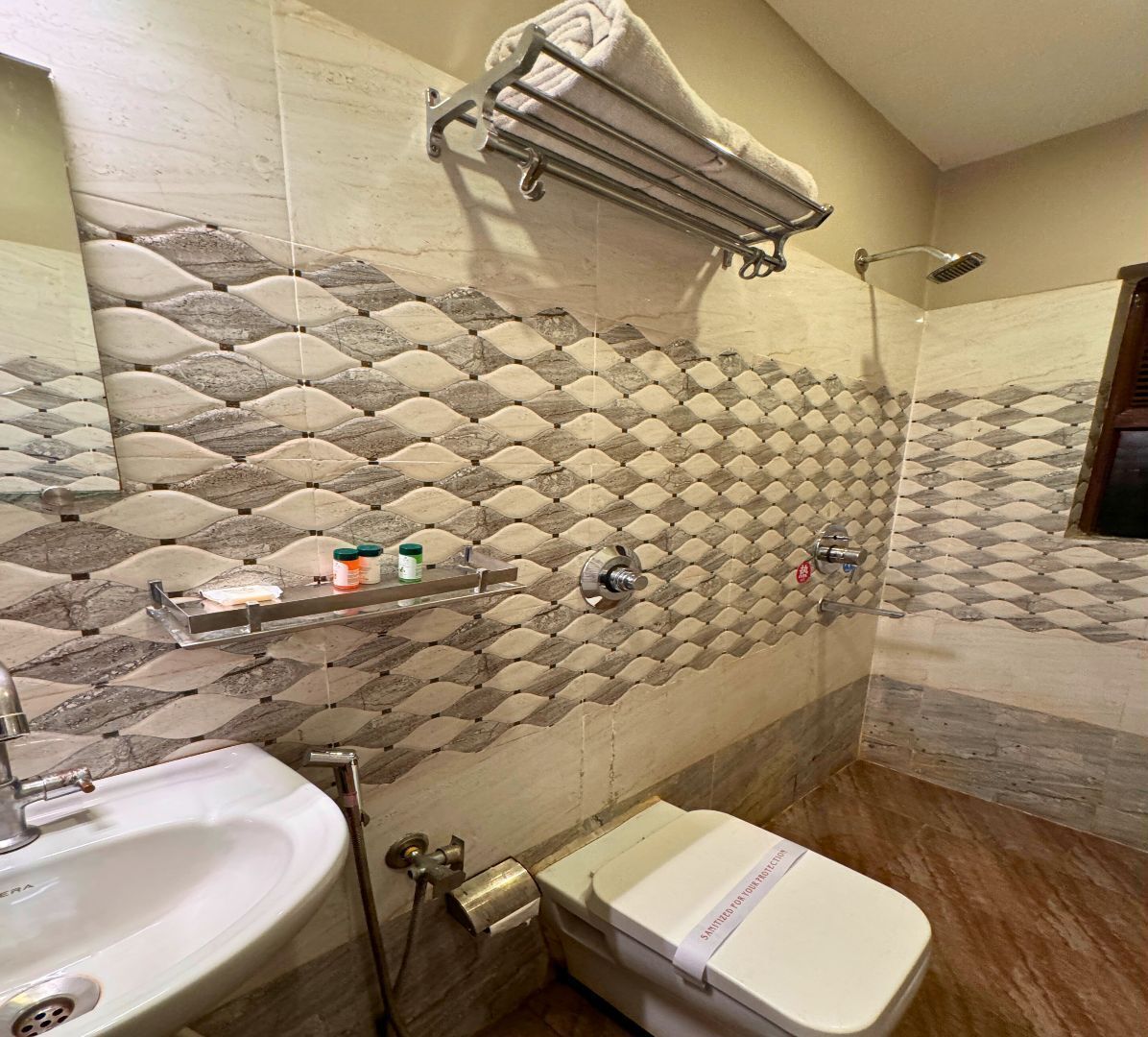 Une salle de bain avec un mur recouvert de carreaux à motifs, un porte-serviettes, une douche et des toilettes.