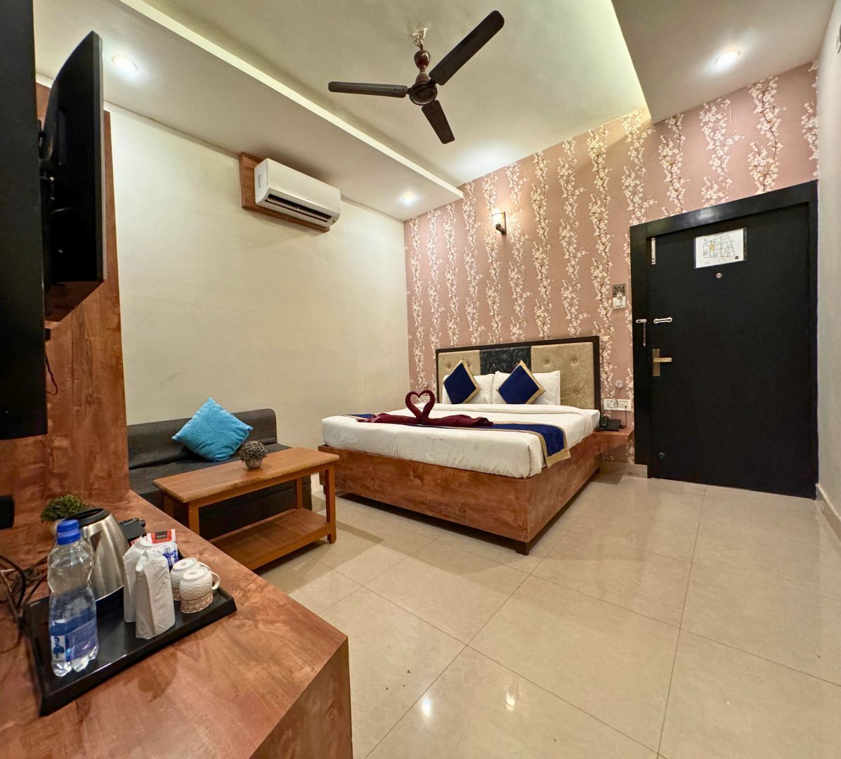 A hotel room with a bed, a desk with a computer, a ceiling fan, and a door.