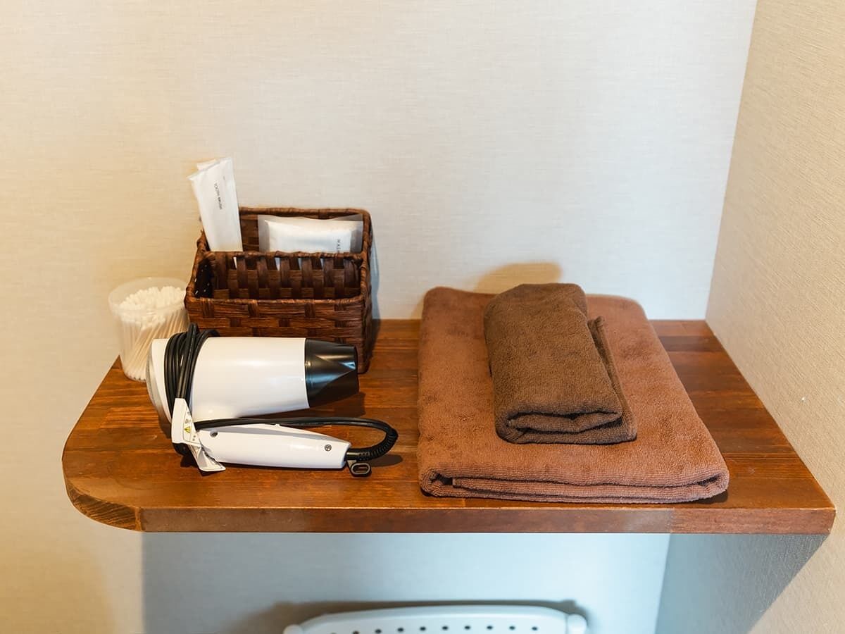 Een houten toonbank met een haardroger, een handdoek en een mand met toiletartikelen.