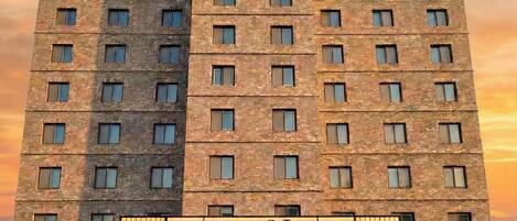 Un hotel de varios pisos con un llamativo letrero 'HOTEL' en la parte superior, una entrada amplia con zona de estacionamiento y fachada de ladrillo.