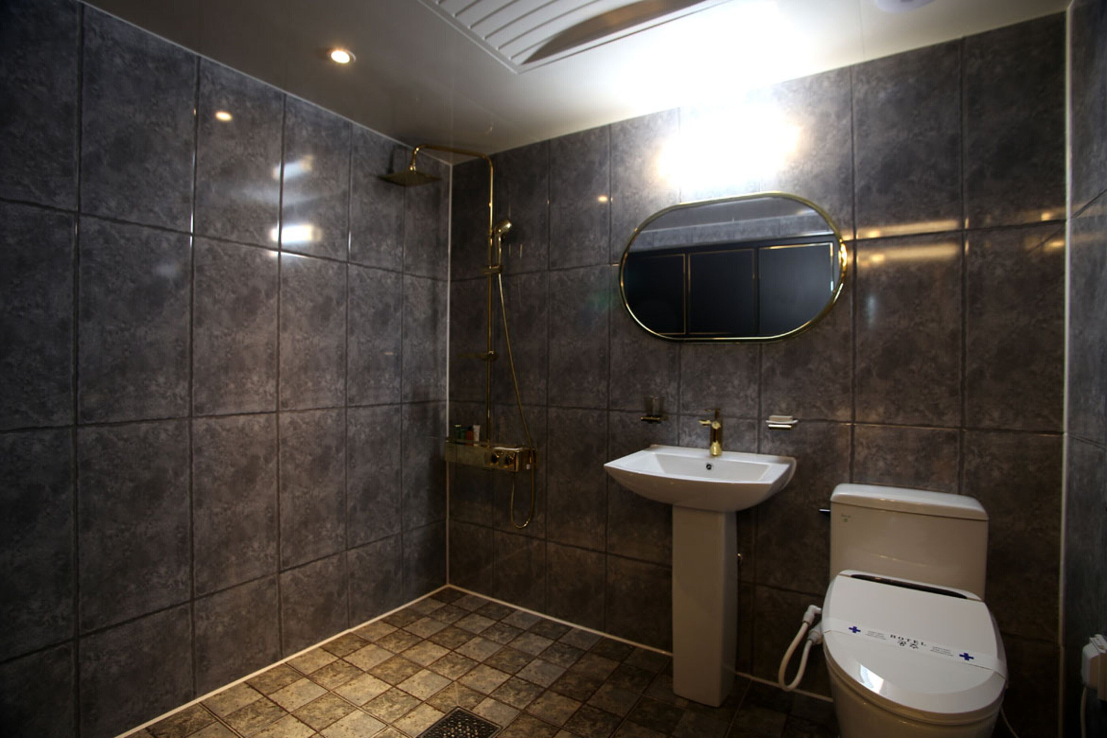 A modern bathroom with dark tiles, a shower, a sink, and a toilet.