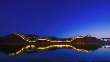A nighttime view of a calm lake with illuminated structures on the hills.