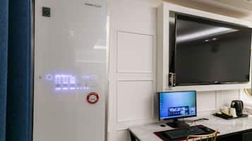 A modern kitchen with a built-in LG refrigerator, a flat-screen TV mounted above the counter, and a computer setup with a monitor, keyboard, and mouse.