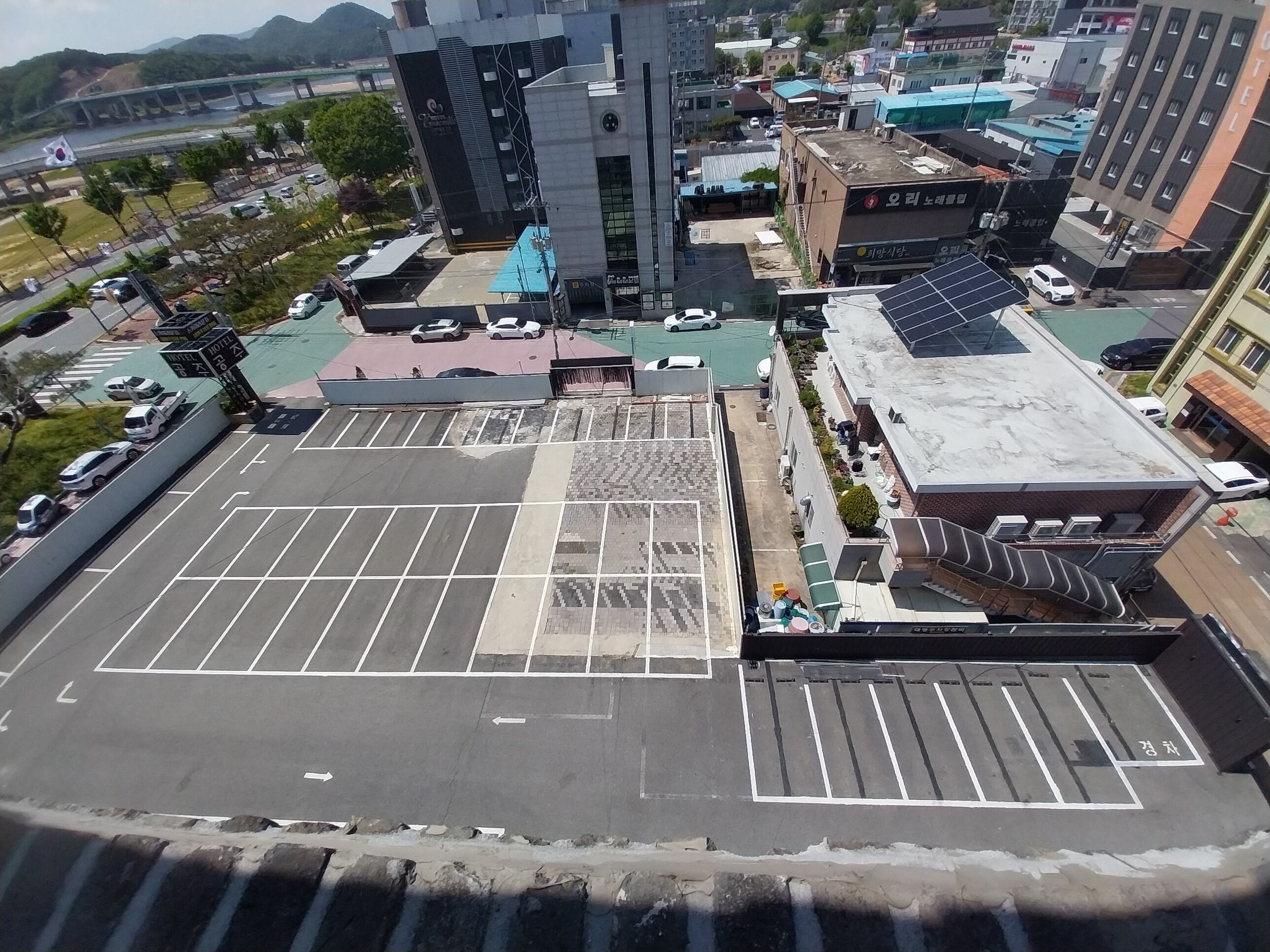 Un área de estacionamiento en la azotea con espacios delimitados, un edificio con un letrero y un puente al fondo.
