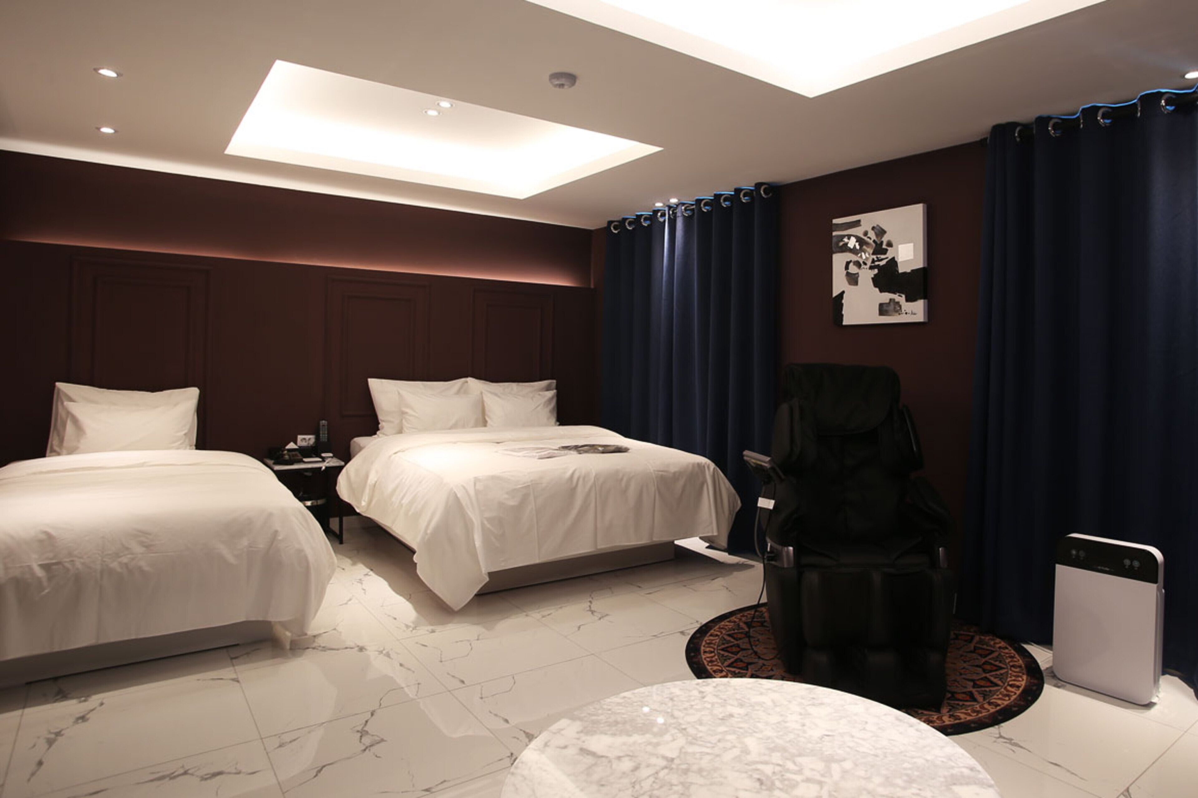A hotel room with two beds, a desk, a chair, a round table, and a ceiling light.
