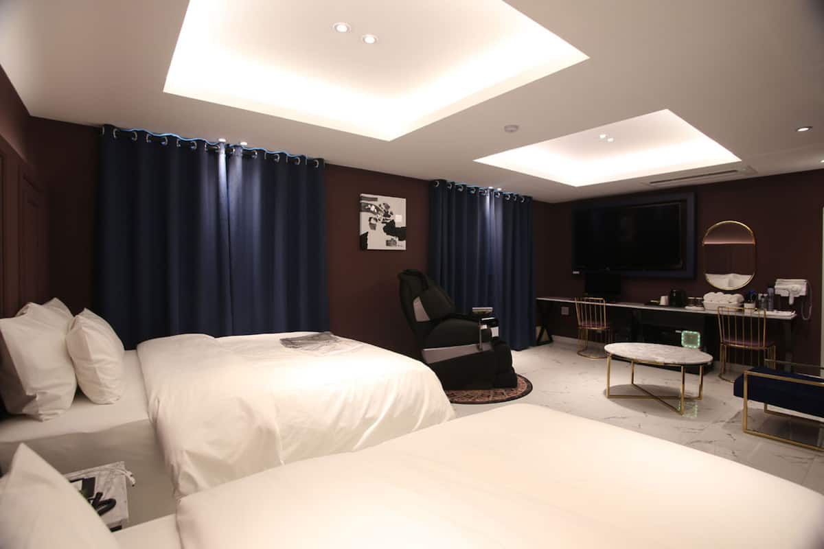 Quarto de hotel com duas camas, uma escrivaninha, uma cadeira, uma televisão e um espelho.