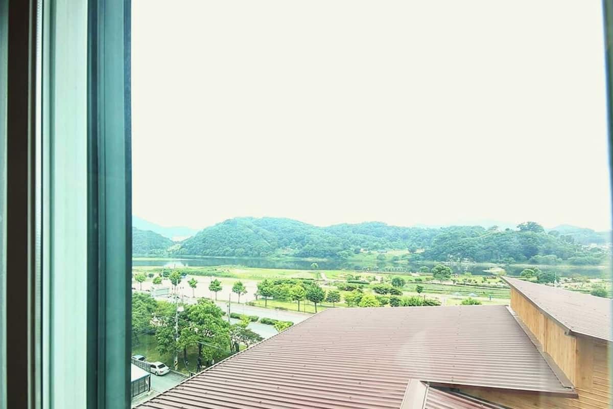 Vista da janela sobre paisagem verde com colinas e céu limpo.