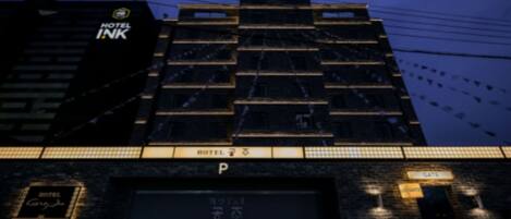 Un edificio de hotel con varios pisos, un letrero llamativo en la parte superior y un cartel que indica un área de estacionamiento.