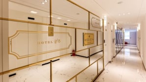 Un pasillo de hotel de diseño moderno, con suelo de mármol y paneles de vidrio con marcos dorados.