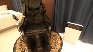 A massage chair in a hotel room with a bed and a control panel.
