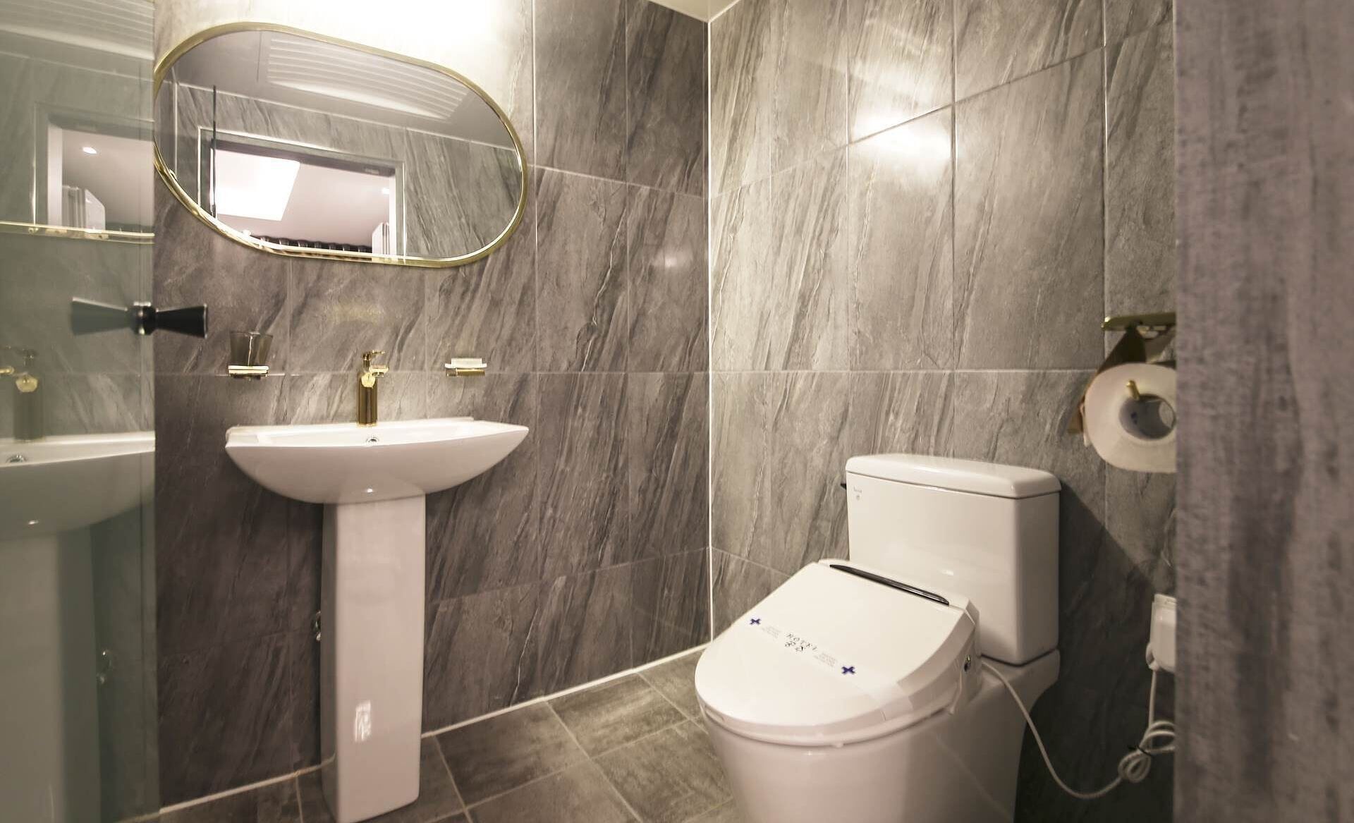 A bathroom with a pedestal sink, a toilet, and a mirror.