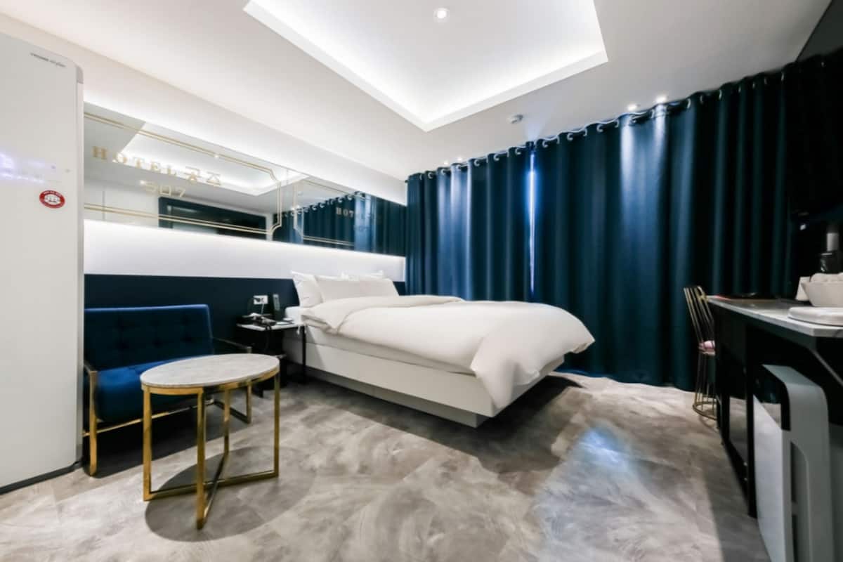 Quarto de hotel moderno com uma cama, uma mesa redonda, uma cadeira, uma escrivaninha e um espelho.