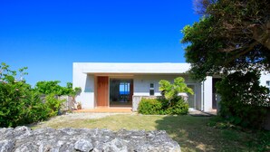 Une maison moderne avec un mur de pierre au premier plan, une porte en bois et un ciel bleu dégagé.