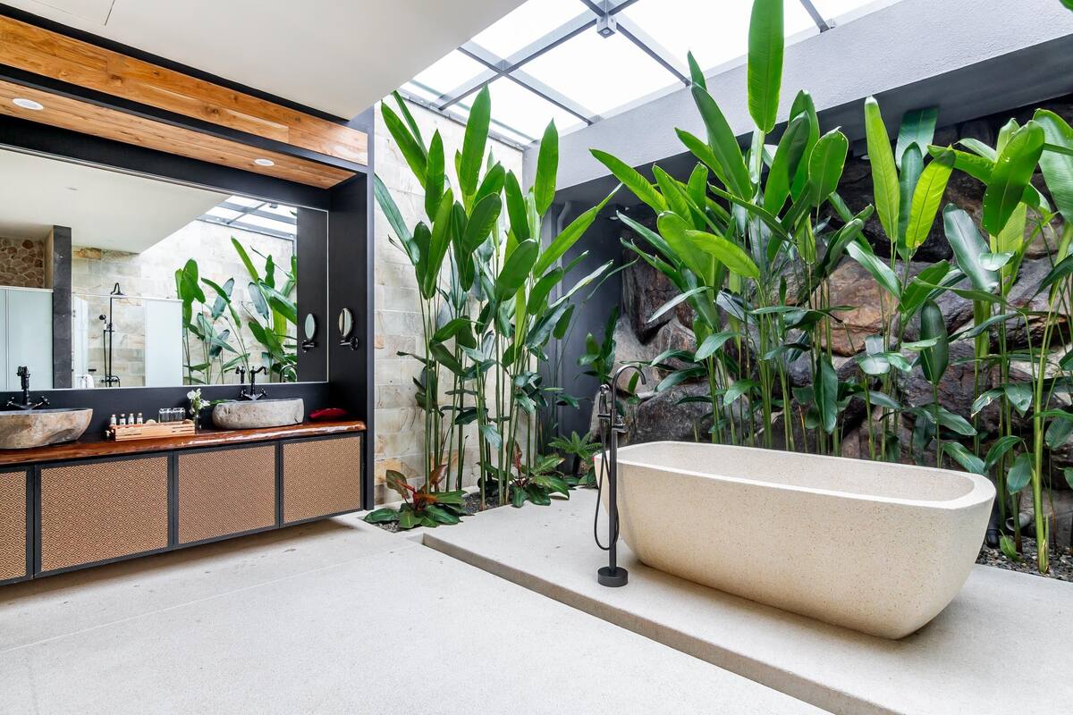 Un baño moderno con una bañera independiente, un espejo grande y varias plantas.