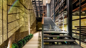 Un escalier avec une rampe en métal menant à un deuxième étage, entouré d’étagères et d’un mur en briques.