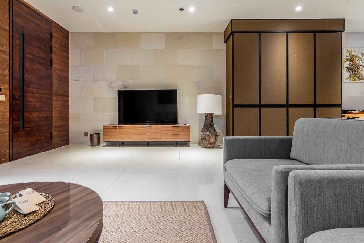 Una sala de estar moderna con un televisor de pantalla plana, un sofá gris, armarios de madera y una lámpara decorativa.